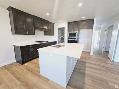 Kitchen featuring light wood-type flooring, a kitchen island with sink, stainless steel appliances, decorative backsplash, and sink | Image 3