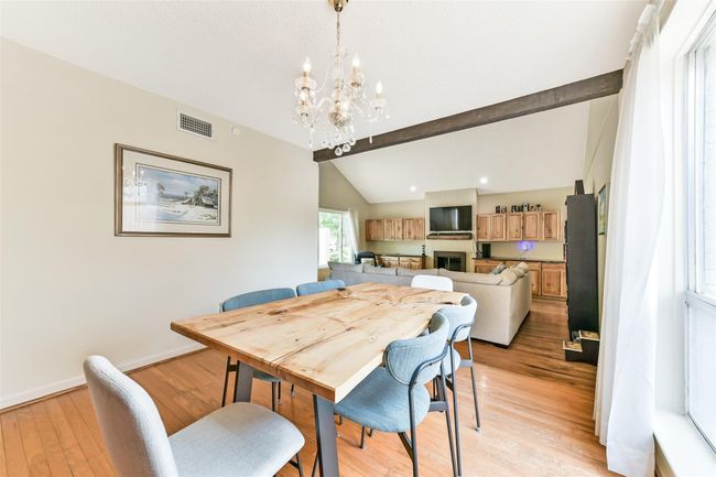 This spacious, open-concept living and dining area features a high ceiling with exposed beams. | Image 13
