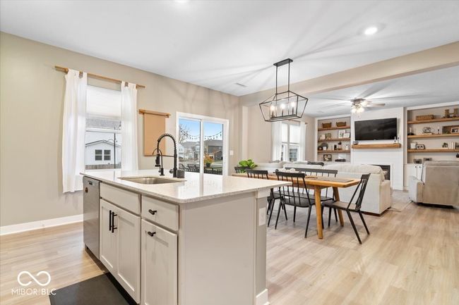 kitchen featuring a fireplace, light wood-style floors, dishwasher, light stone countertops, and hanging light fixtures | Image 14