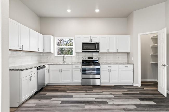 Gourmet kitchen with light stone countertops, white cabinetry, stainless steel appliances, and dark wood-type flooring | Image 9