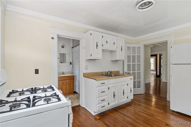 Kitchen with white appliances, wood finished floors, white cabinetry, light countertops, and crown molding | Image 40