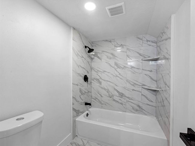 This bathroom features a sleek design with white marble-look tile surrounding a bathtub and shower area. It has modern black fixtures and a simple, clean aesthetic, perfect for a contemporary home. | Image 28