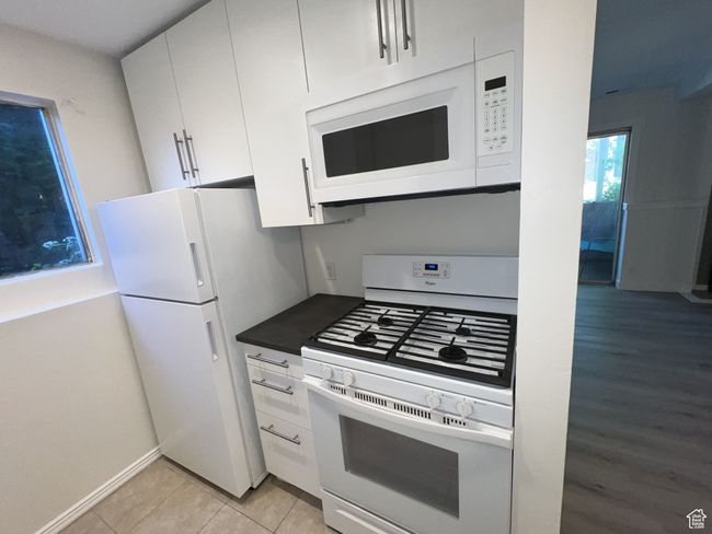 Kitchen with white appliances, white cabinetry, dark countertops, baseboards, and light tile patterned flooring | Image 5