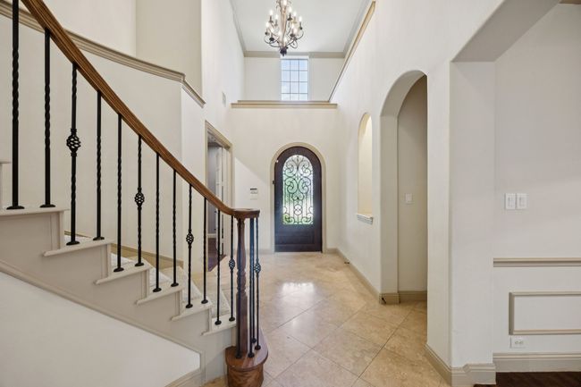 Tiled entrance foyer featuring a chandelier, baseboards, arched walkways, a high ceiling, and stairs | Image 6