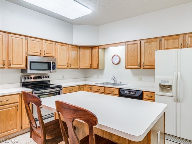 Kitchen featuring brown cabinets, light countertops, stainless steel appliances, and light tile floors | Image 15