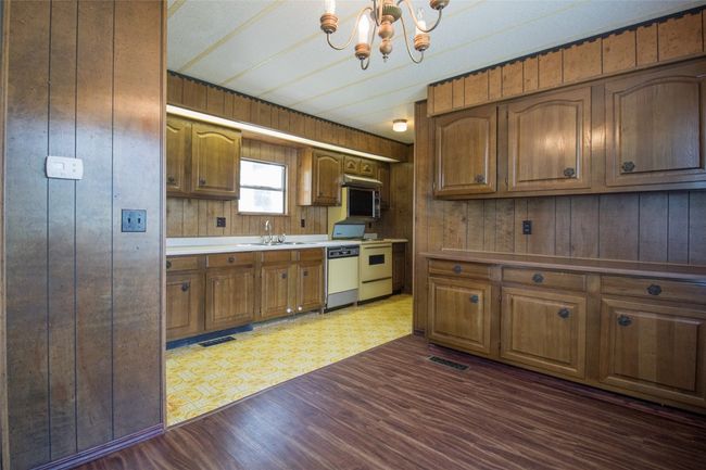 Kitchen featuring dishwashing machine, wooden walls, a chandelier, brown cabinetry, and dark wood-type flooring | Image 12