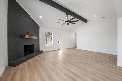 Unfurnished living room with light hardwood / wood-style flooring, a brick fireplace, lofted ceiling with beams, and ceiling fan | Image 3