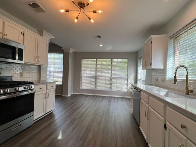 Kitchen featuring decorative backsplash, appliances with stainless steel finishes, dark wood-style flooring, white cabinetry, and recessed lighting | Image 14