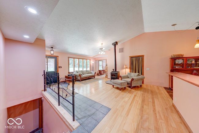 living room featuring a wood stove, light wood-style flooring, lofted ceiling, a textured ceiling, and ceiling fan | Image 52