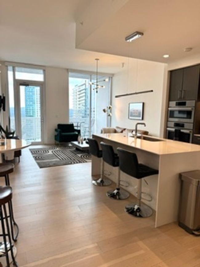 Kitchen featuring a kitchen bar, a sink, stainless steel double oven, light countertops, and an island with sink | Image 10