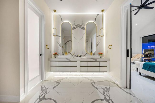 Step into spa-like sophistication in this luxurious en suite primary bathroom, featuring dramatic book-matched marble tile, designer pendant lighting, and floating vanity with integrated LED backlighting. Gold accents add a touch of opulence, while the seamless layout offers both style and serenity—your daily retreat redefined. | Image 23