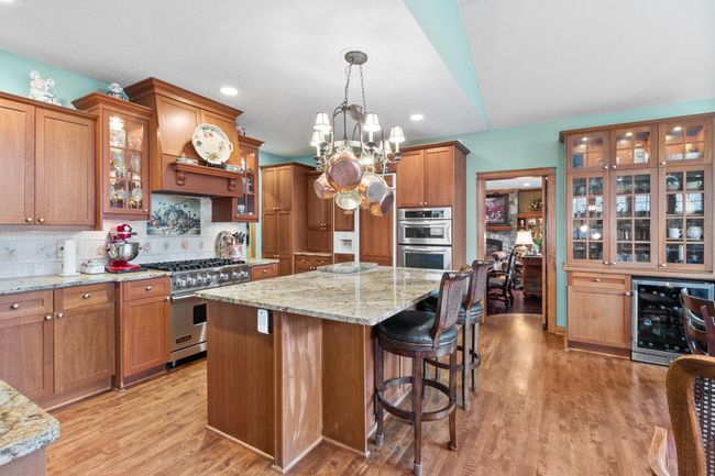 Kitchen showing vent-a-hood over Viking stove. View toward butler door to formal dining and wine refrigerator featuring lighted glass storage and display cabinet. | Image 8