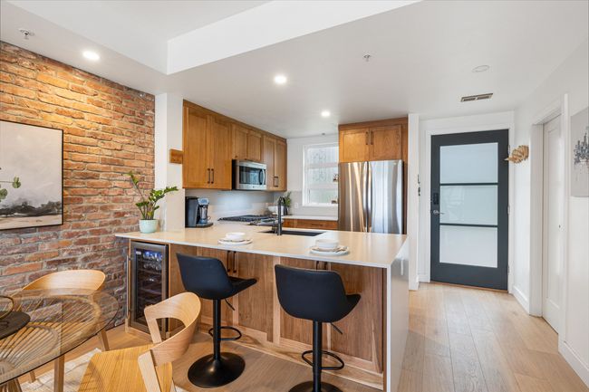 Kitchen featuring stainless steel appliances, wine cooler, a peninsula, light wood-style flooring, and light countertops | Image 4