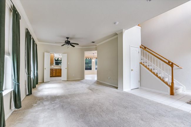 Unfurnished living room with crown molding, a ceiling fan, light carpet, stairs, and a chandelier | Image 4
