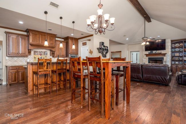 Dining area with a ceiling fan, dark wood finished floors, a stone fireplace, a chandelier, and recessed lighting | Image 13