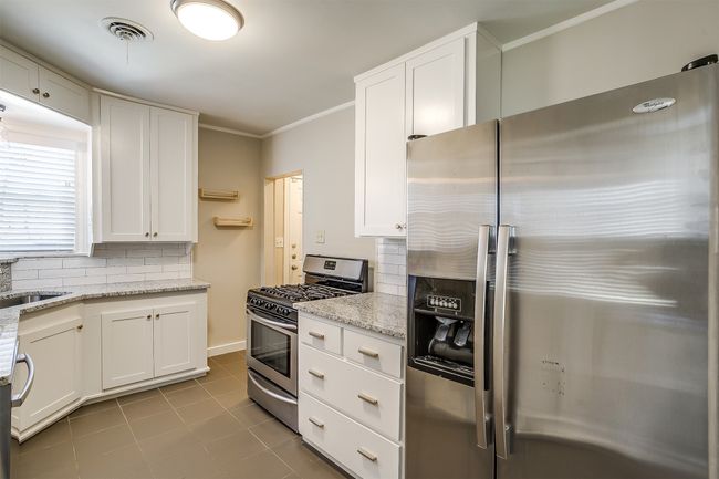 Kitchen featuring stainless steel appliances, white cabinets, tasteful backsplash, ornamental molding, and light stone countertops | Image 8