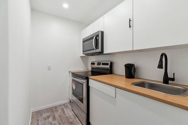 Kitchen featuring baseboards, light wood-type flooring, white cabinets, stainless steel appliances, and a sink | Image 27