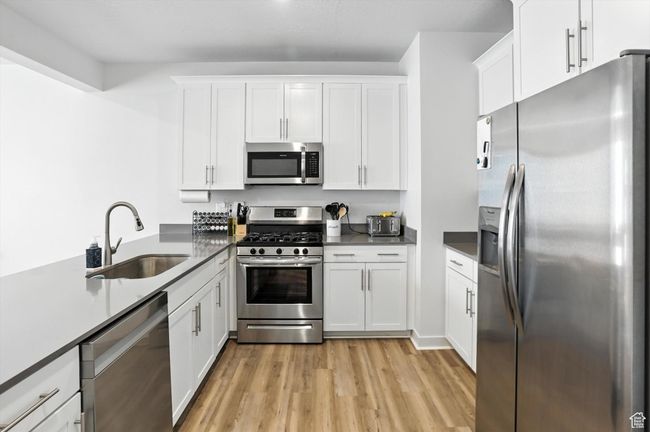 Kitchen featuring stainless steel appliances, new light wood-style LVP floors, white cabinetry, and dark grey quarts countertops | Image 9