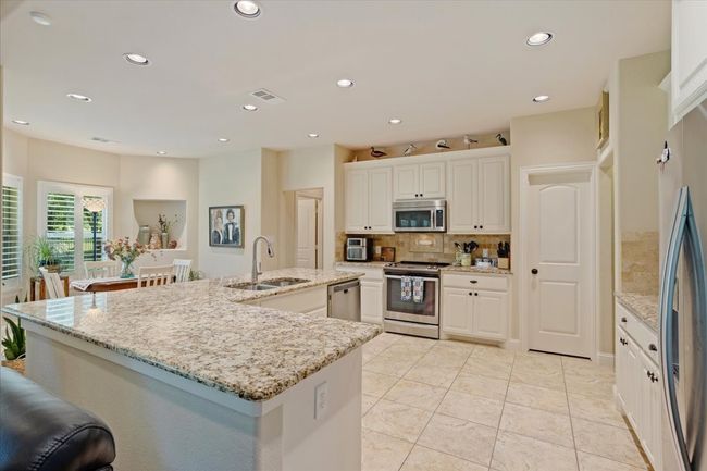Kitchen featuring stainless steel appliances, a sink, backsplash, a large island, and white cabinets | Image 8