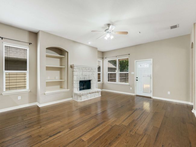 Unfurnished living room with a ceiling fan, wood-type flooring, a fireplace, and built in shelves | Image 8