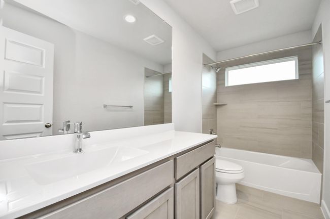 Secondary bath features tile flooring, bath/shower combo with tile surround, light stained wood cabinets, beautiful light countertop. | Image 35