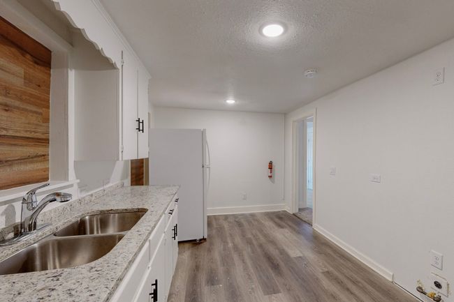 Kitchen featuring light stone counters, white refrigerator, sink, and white cabinets | Image 13