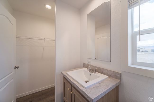 Bathroom with vanity, a walk in closet, wood finished floors, and baseboards | Image 9