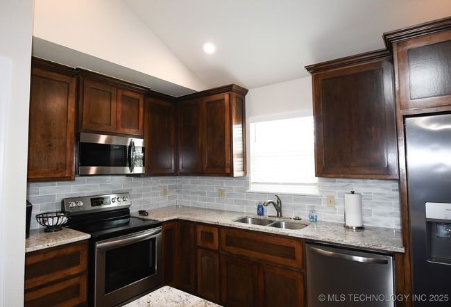 Kitchen featuring stainless steel appliances, a sink, backsplash, vaulted ceiling, and light stone countertops | Image 15