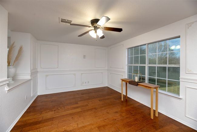 Dining room featuring visible vents, engineered wood finished floors, a ceiling fan, and a decorative wall | Image 8