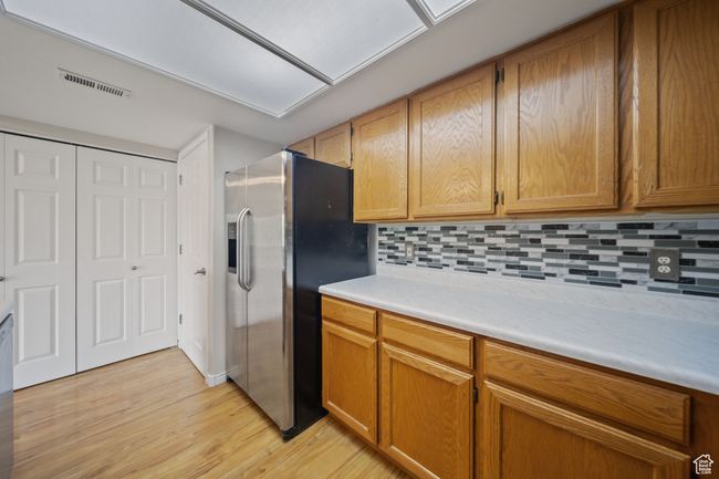 Kitchen with stainless steel fridge with ice dispenser, light wood-type flooring, light countertops, backsplash, and brown cabinetry | Image 9