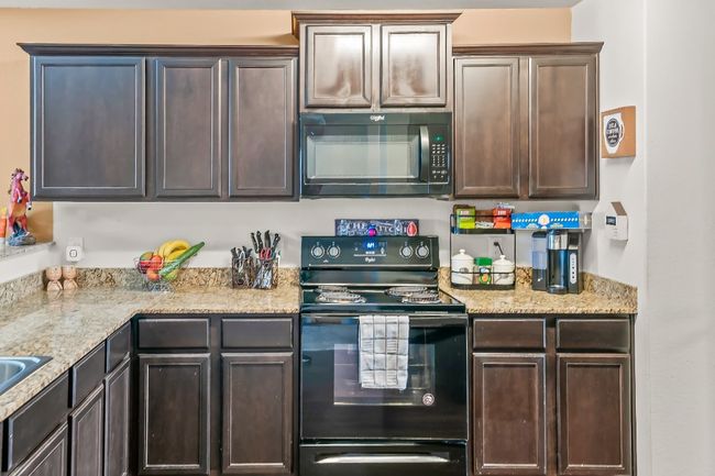 Kitchen with light stone counters, dark brown cabinetry, and black appliances | Image 7