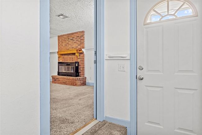 Foyer entrance with a textured ceiling, carpet flooring, a brick fireplace, and brick wall | Image 9