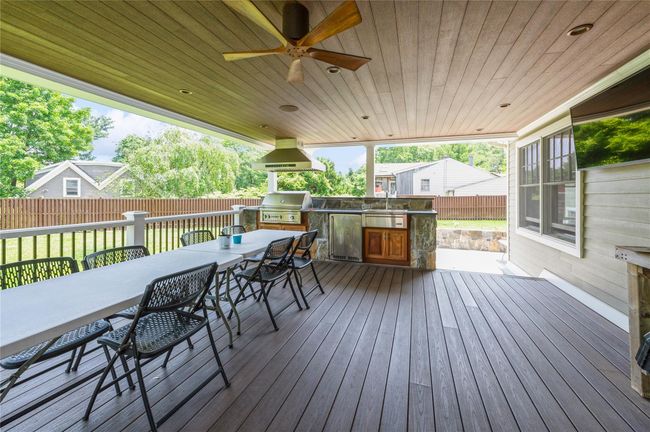 Exterior covered deck featuring kitchen, outdoor dining space, a fenced backyard, and ceiling fan | Image 17