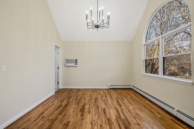 Unfurnished dining area with wood-type flooring, a notable chandelier, high vaulted ceiling, and a baseboard heating unit | Image 19