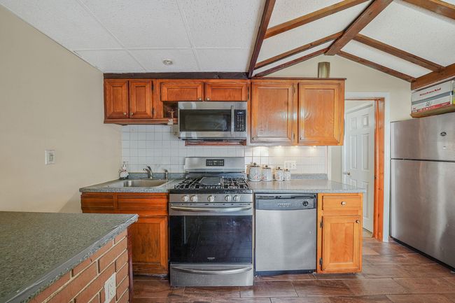 Kitchen featuring stainless steel appliances, a sink, backsplash, lofted ceiling, and brown cabinetry | Image 15