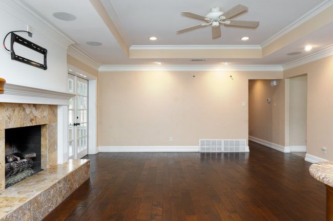 Unfurnished living room with dark wood finished floors, a premium fireplace, a ceiling fan, crown molding, and a raised ceiling | Image 12
