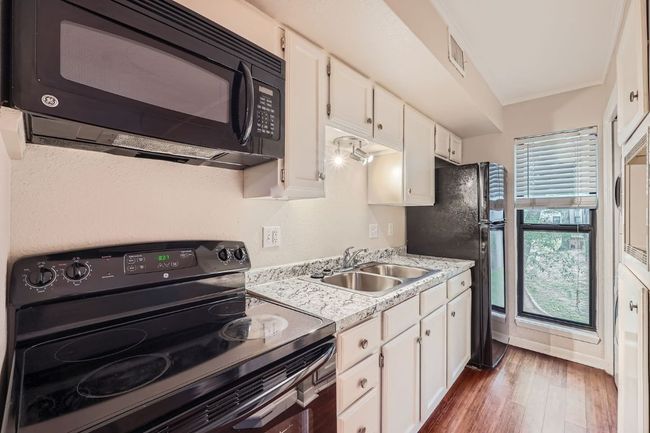 Kitchen featuring white cabinetry, a sink, black appliances, and wood finished floors | Image 7