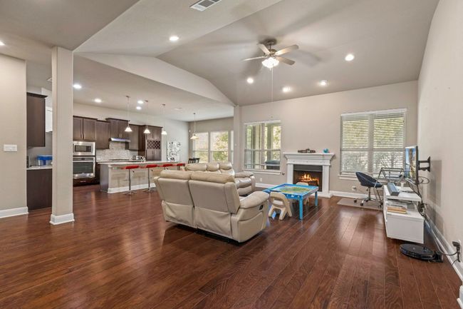 Living area featuring ceiling fan, dark wood-style floors, vaulted ceiling, a warm lit fireplace, and recessed lighting | Image 7