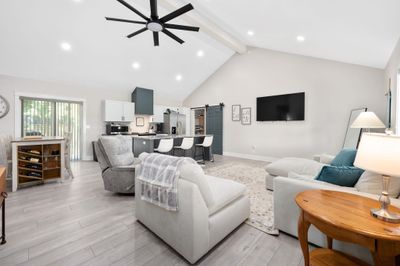 Living room featuring light wood-type flooring, ceiling fan, a barn door, and beamed ceiling | Image 3