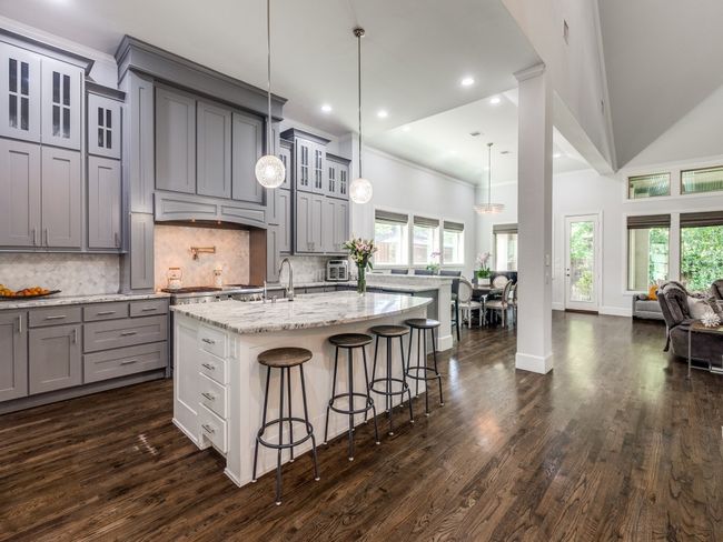 Kitchen with gray cabinets, a center island with sink, open floor plan, a breakfast bar, and dark wood-style flooring | Image 5
