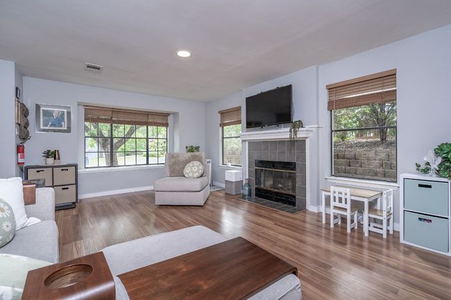 Living room featuring wood finished floors, a healthy amount of sunlight, a tiled fireplace, baseboards, and visible vents. | Image 8