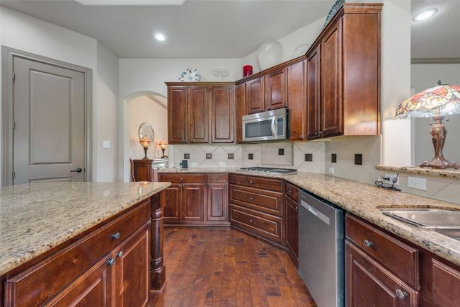 Kitchen with appliances with stainless steel finishes, dark wood finished floors, light stone counters, backsplash, and arched walkways | Image 21