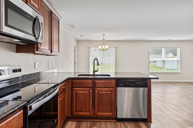 Kitchen with stainless steel appliances, a peninsula, a chandelier, dark wood-style floors, and dark stone counters | Image 10