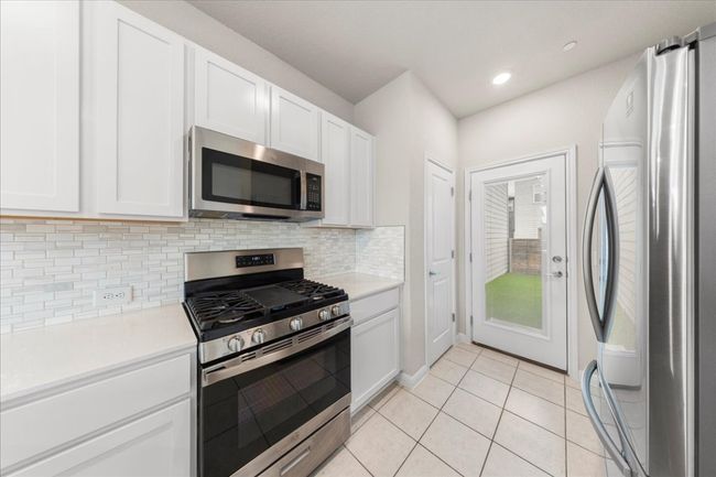 Kitchen with stainless steel appliances, light countertops, white cabinets, backsplash, and light tile patterned floors | Image 12
