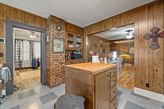 Kitchen with a ceiling fan, wood walls, butcher block countertops, a textured ceiling, and brown cabinets | Image 10