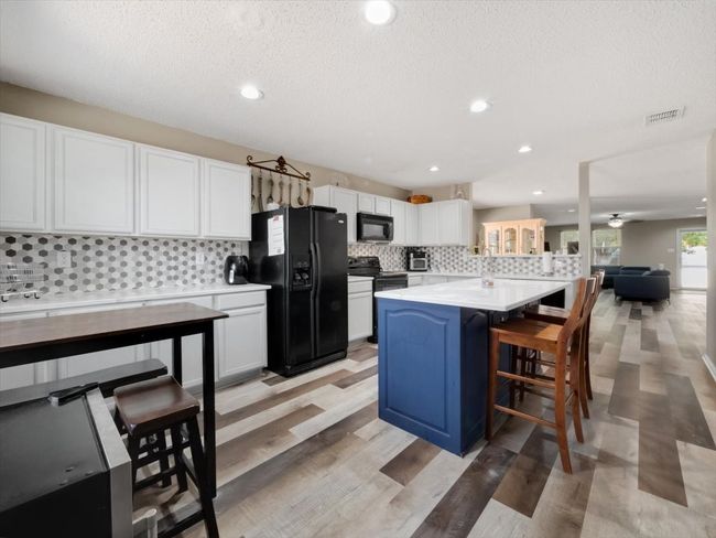 Kitchen with a textured ceiling, black appliances, a center island, a kitchen bar, and white cabinetry | Image 9