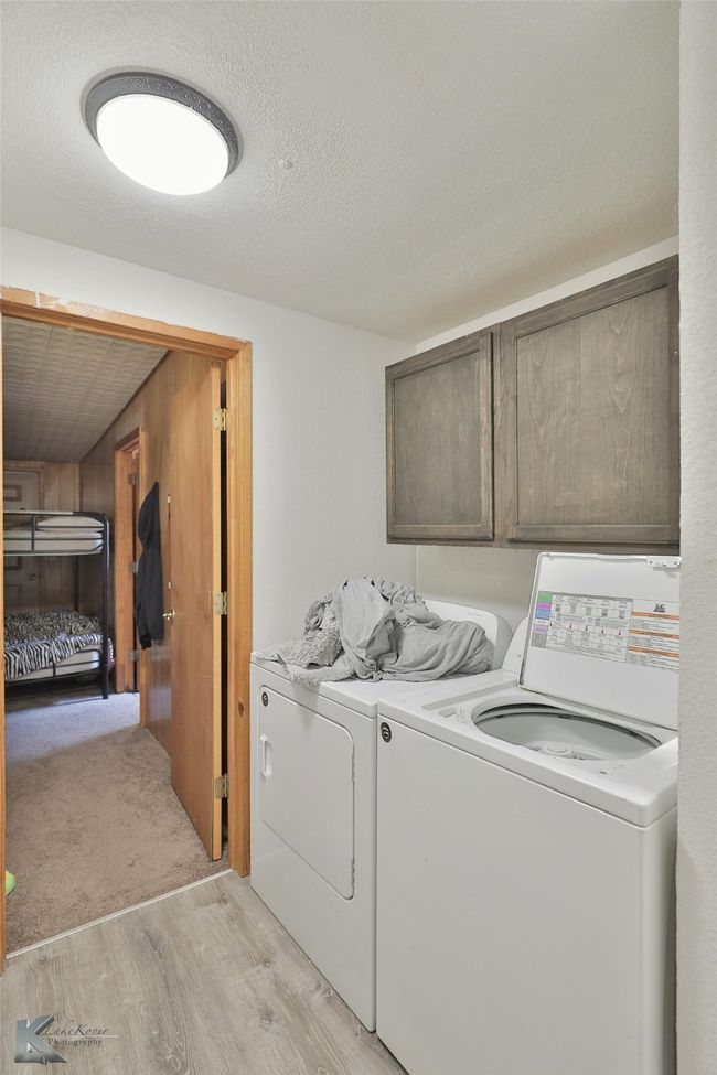 Washroom with a textured ceiling, washing machine and dryer, cabinet space, and light wood-style flooring | Image 24