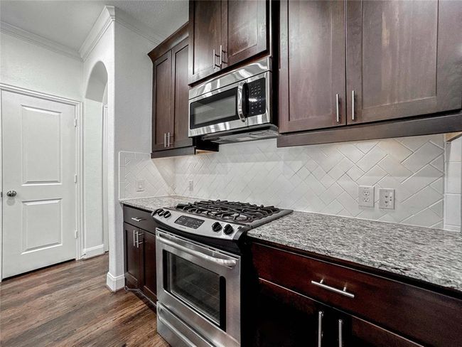This kitchen features dark wood cabinetry, a sleek granite countertop, stainless steel appliances, and a stylish white subway tile backsplash, offering a modern and functional space. | Image 10