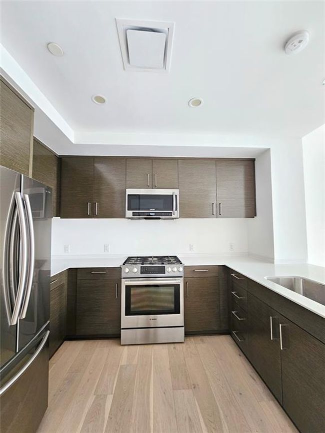 Kitchen with dark brown cabinetry, modern cabinets, light countertops, light wood-style flooring, and stainless steel appliances | Image 4