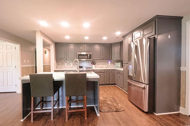 Kitchen with appliances with stainless steel finishes, gray cabinets, light countertops, a center island with sink, and decorative backsplash | Image 5